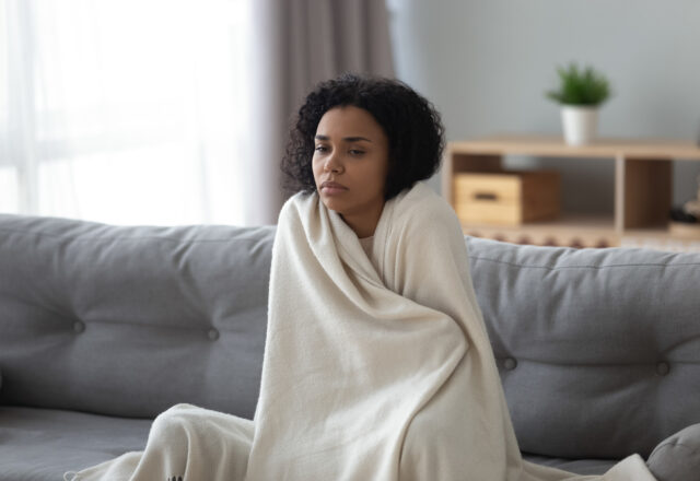 Sick woman feeling cold covered with blanket at home