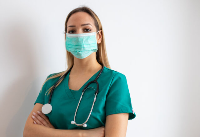 Female nurse standing arms crossed. Confident young woman doctor. Female nurse young pretty woman in green clothes with medical mask posing.