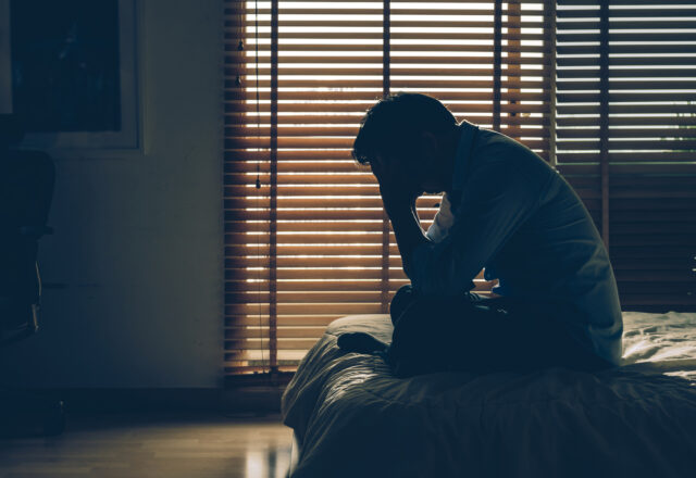 Sad businessman sitting head in hands on the bed in the dark bedroom with low light environment, dramatic concept, vintage tone color