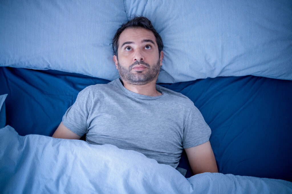 Anxious man trying to sleep but suffering insomnia