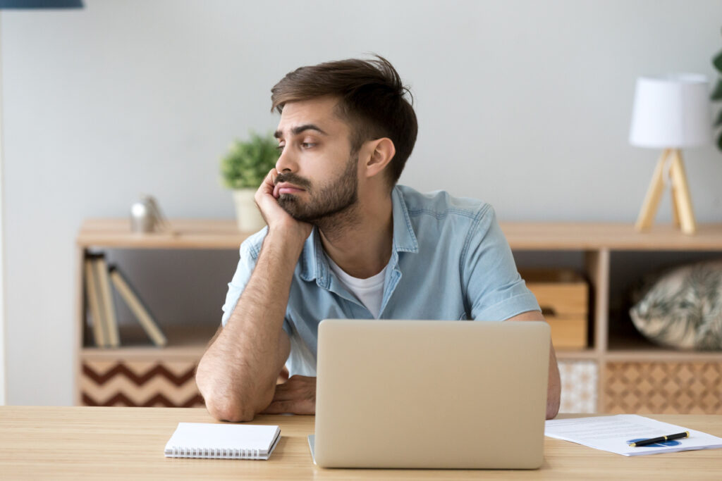 Tired man distracted from computer work lacking motivation