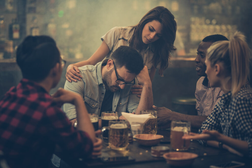 Group of friends consoling their friend who is sitting drunk in a bar.