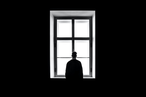 Man standing alone in front of a lit up window.