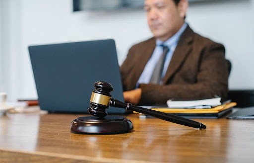 A gavel with a man typing on a computer in the background.